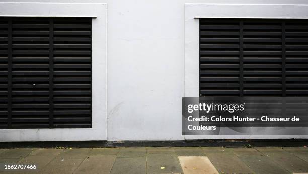 white painted concrete wall with two wide black metal grilles for ventilation in london, england, united kingdom. paved and weathered sidewalk. - lawn aeration stock pictures, royalty-free photos & images