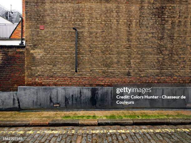 weathered brown brick and grey cement wall with sidewalk and paved street in london, england, united kingdom. no people. - cobblestone floor stock pictures, royalty-free photos & images