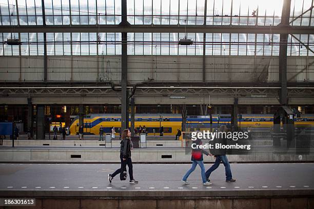 Commuters pass along a platform as a Koploper passenger train, operated by Nederlandse Spoorwegen, stands beyond at Amsterdam Centraal station in...