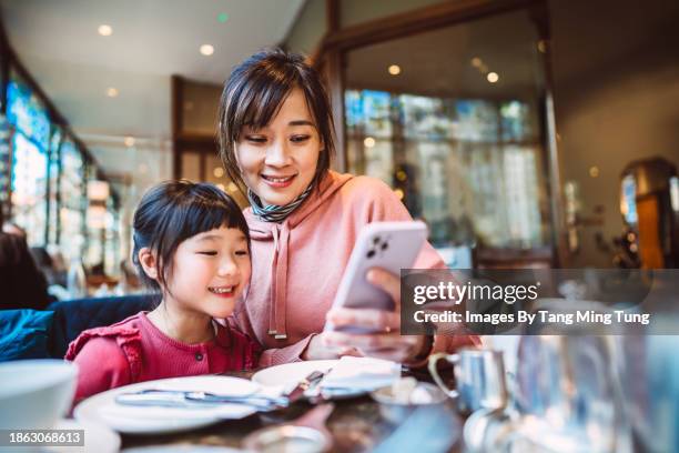 mom & daughter using smart phone together while enjoying traditional afternoon tea in restaurant - tea shop stock pictures, royalty-free photos & images