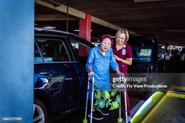 elderly woman using mobility walker in parking garage with nurse home caregiver's assistance - assisted living community stock pictures, royalty-free photos & images