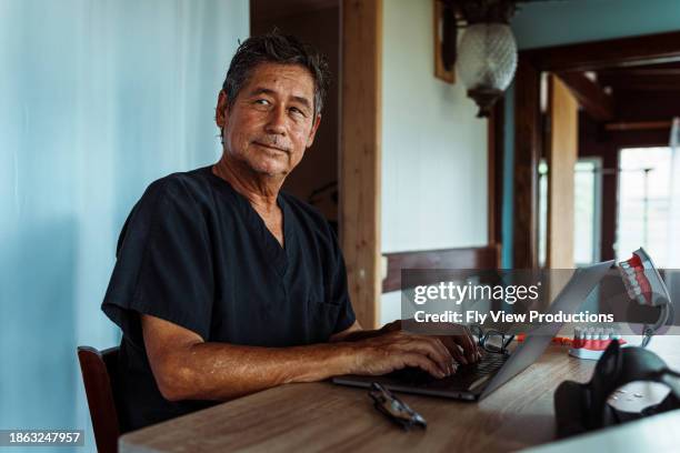 male dentist types on computer in home office - insulano do pacífico imagens e fotografias de stock