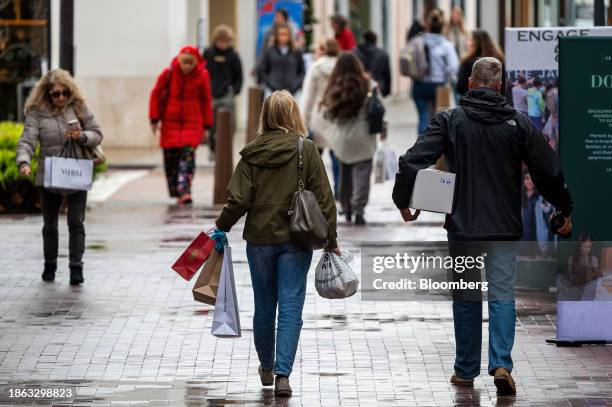 Shoppers carry bags in Walnut Creek, California, US, on Wednesday, Dec. 20, 2023. US retail sales unexpectedly picked up in November as lower...