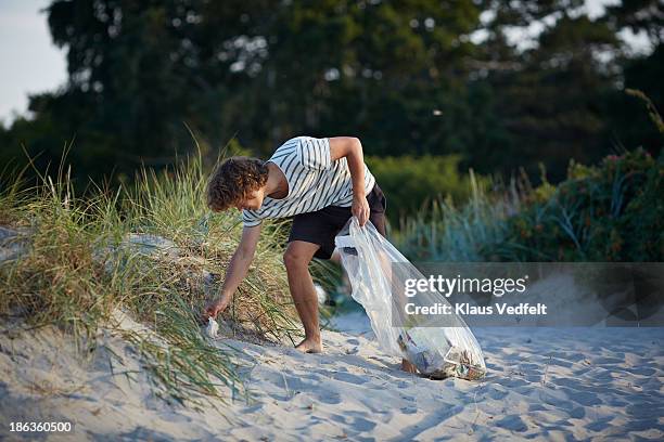 young man collecting trash on beach - environmental cleanup stock pictures, royalty-free photos & images
