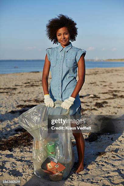 cute young woman holding trash bag on beach - volunteer beach photos et images de collection