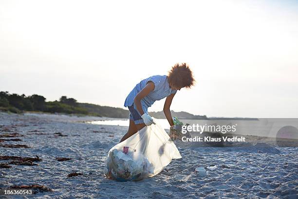 young woman collecting trash on beach - volunteer beach photos et images de collection