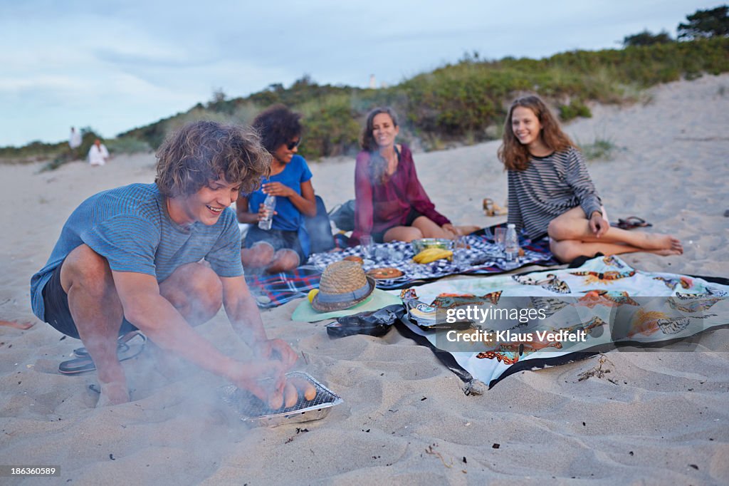 Young man putting sausages on smoking grill