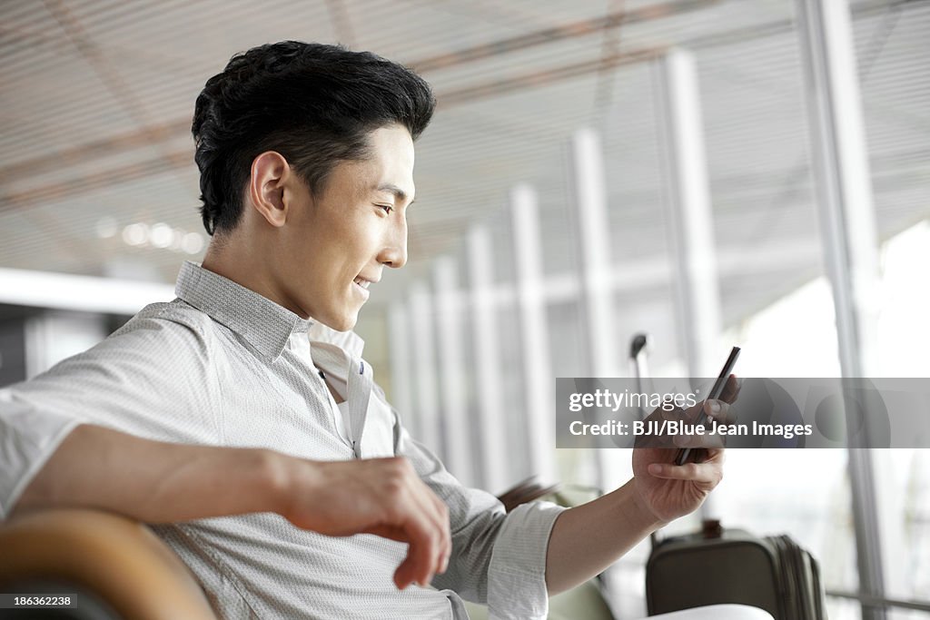 Young man with smart phone waiting in airport lounge