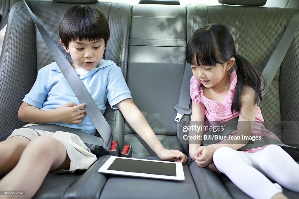 Cute boy and girl playing digital tablet in car