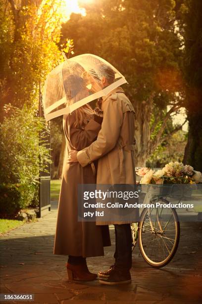 caucasian couple hugging under umbrella - couples kissing shower stockfoto's en -beelden