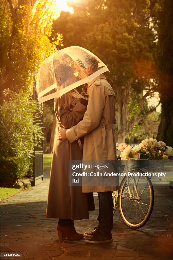 Caucasian couple hugging under umbrella