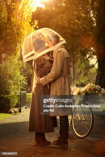 caucasian couple hugging under umbrella - sharing umbrella stock pictures, royalty-free photos & images