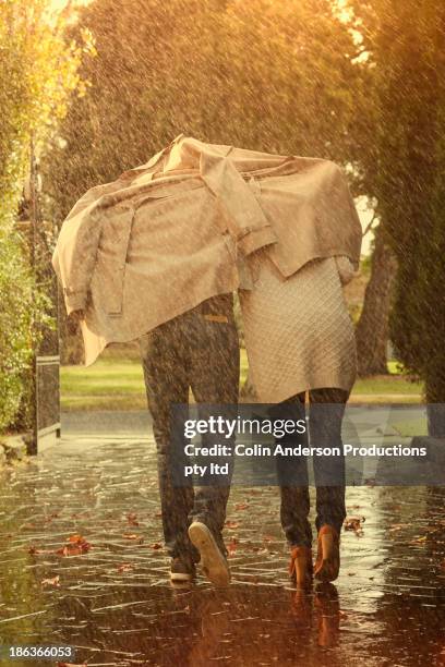 caucasian couple running under coat in rain - rain couple stockfoto's en -beelden