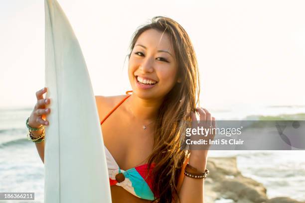 mixed race woman holding surfboard on beach - ボード　持つ　女性 ストックフォトと画像