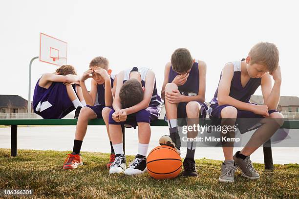 caucasian basketball team sulking by court - subdue stockfoto's en -beelden