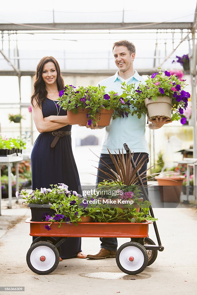 Caucasian couple carrying potted flowers in plant nursery