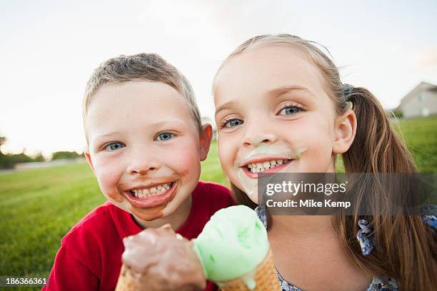 caucasian children eating ice cream outdoors - girl sitting on boys face fotografías e imágenes de stock