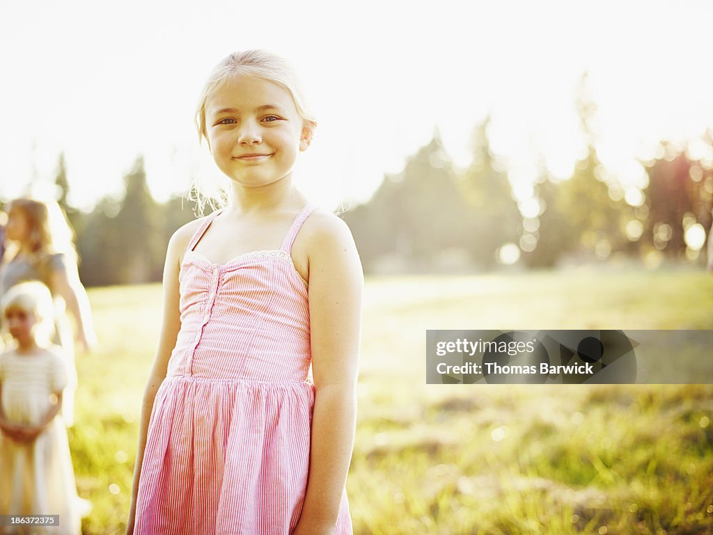 Smiling young girl standing in field at sunset