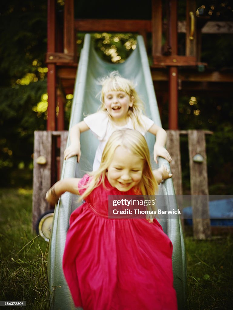 Smiling young girls riding down slide laughing