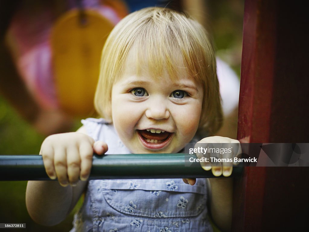 Smiling young toddler holding onto bar of playset