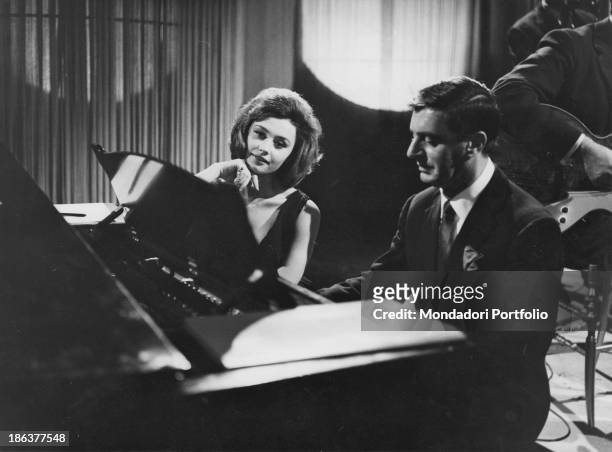 Italina TV host, actor and singer Lelio Luttazzi playing piano while Italian TV host, actress, singer and showgirl Raffaella Carrà seats beside him...