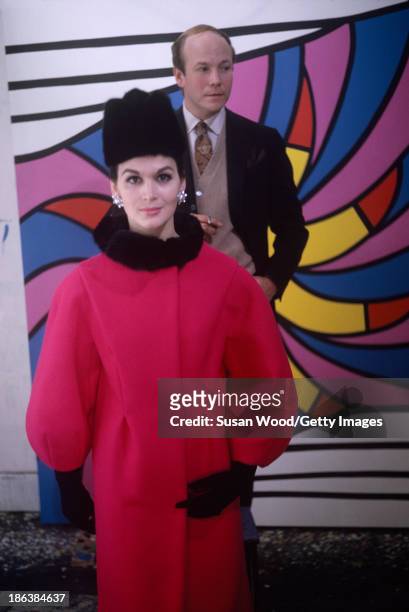 Portrait of Carmen Dell'Orefice in a red coat with a black fur collar, a black hat, and gloves as she poses with an unidentified man in front of a...