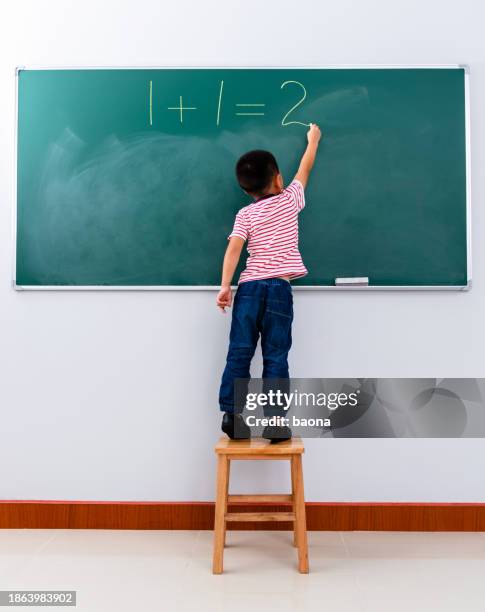 a boy writing 1+1=2 on chalkboard - wiskunde stockfoto's en -beelden