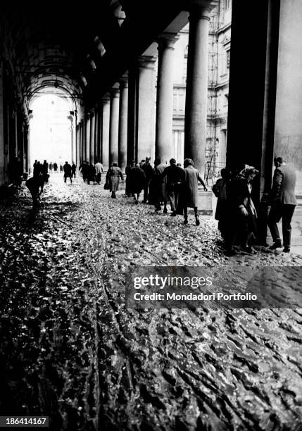 People walking under the porch of Uffizi Gallery full of mud in consequence of the flood of the Arno River. Florence, November 1966.