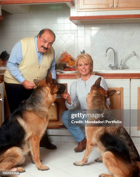 Italian journalist and TV host Maurizio Costanzo feeding two German Shepherds in the kitchen beside his wife and Italian TV presenter Maria De...