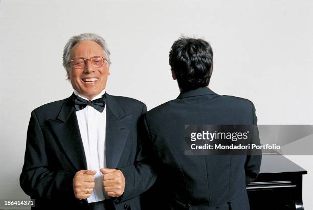 Italian singer-songwriter, stand-up comedian and actor Enzo Jannacci in dinner jacket laughing seated at the piano beside another man. 1990s.