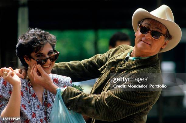 Theatrical broadcast presenter Renzo Arbore laughs at Neapolitan show girl Marisa Laurito's sunglasses, while she smiles amused; the two artists are...