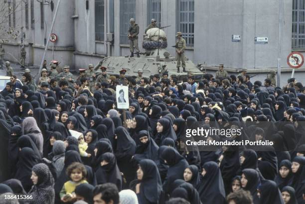 Veiled iranian women parade during the Iranian Revolution under the eyes of the military. A protester supports an image of Ruhollah Khomeyni, the...