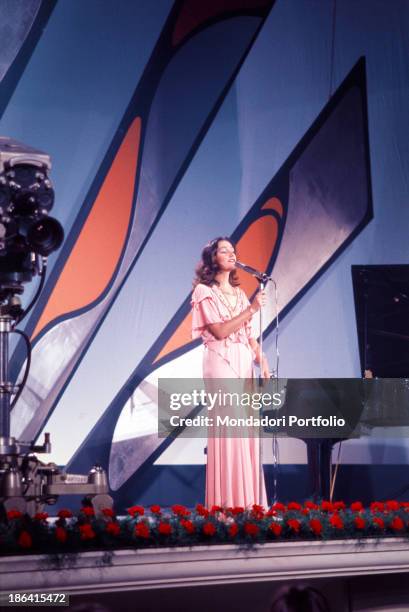 Italian singer Mia Martini singing a song beside a piano wearing a pink dress. 1970s.