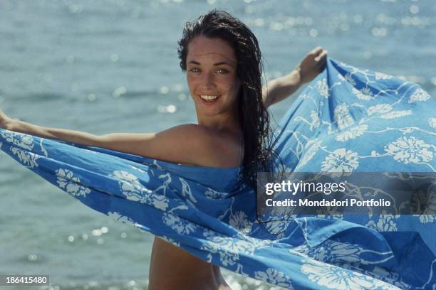 The Italian dancer Oriella Dorella smiles posing with a sarong on a beach in Tahiti. French Polynesia, Tahiti, 1981.