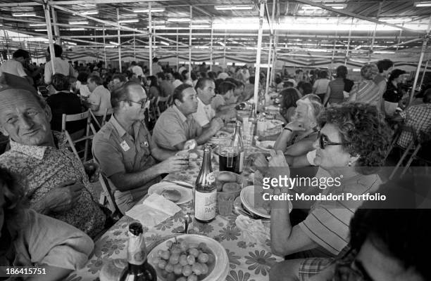 Large group of people eating under a big tent set up on the occasion of the Festa de l'Unità. Bologna, September 1980.