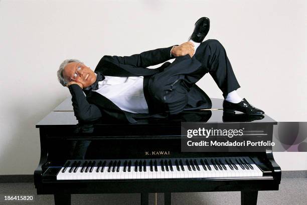 Italian singer-songwriter, stand-up comedian and actor Enzo Jannacci in dinner jacket resting his head on the head while lying on a piano. 1990s.