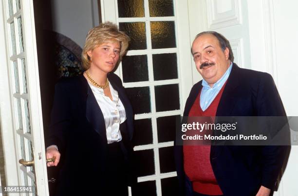 Italian journalist and TV host Maurizio Costanzo smiling beside his future wife and Italian Tv presenter Maria De Filippi leaned on a door handle....