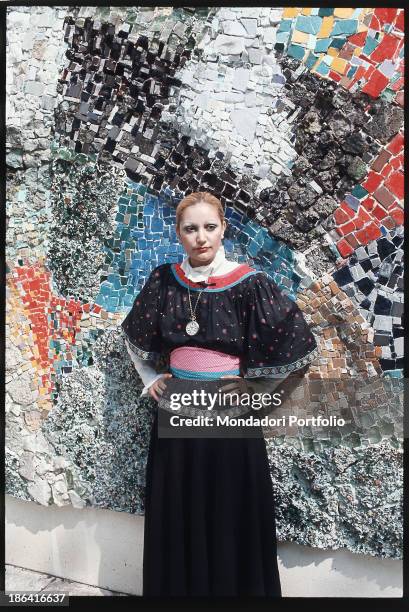 Italian singer Mia Martini posing with her hands on her hips next to a mosaic in the park of the Enzo Pagani Museum. Castellanza, 1972.