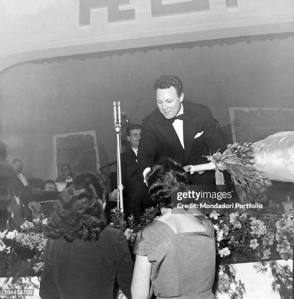 Two women giving a bunch of flowers to Italian singer Claudio Villa who won the 5th Sanremo Music Festival with the song Buongiorno tristezza....