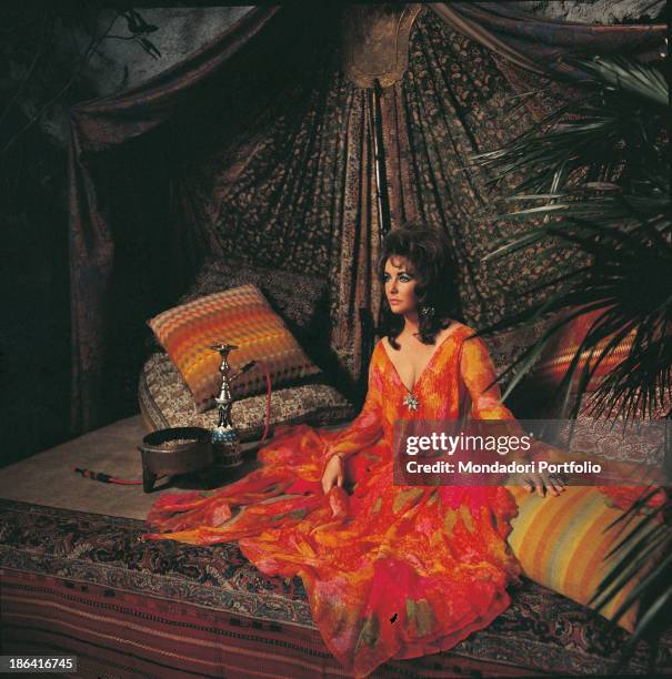 British-born American actress Elizabeth Taylor sitting among oriental cushions and carpets beside a narghile. 1973.