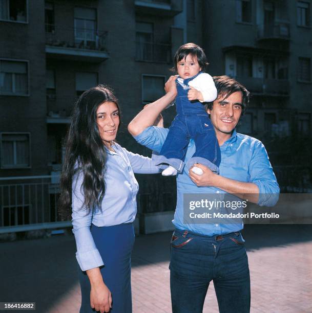 Italian singer-songwriter and writer Roberto Vecchioni smiling with his wife Irene Bozzi holding his daughter Francesca in his arms. Milan, 1976.