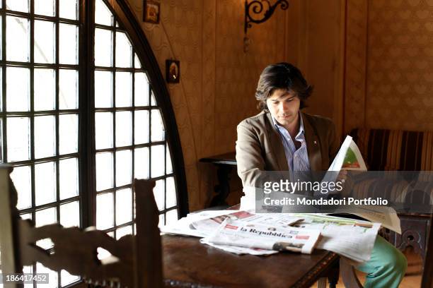 Vittorio Sgarbi's son Carlo Sgarbi Brenner reading the newspaper La Repubblica seated in a room of Villa Banfi. Vimercate, 2000s.