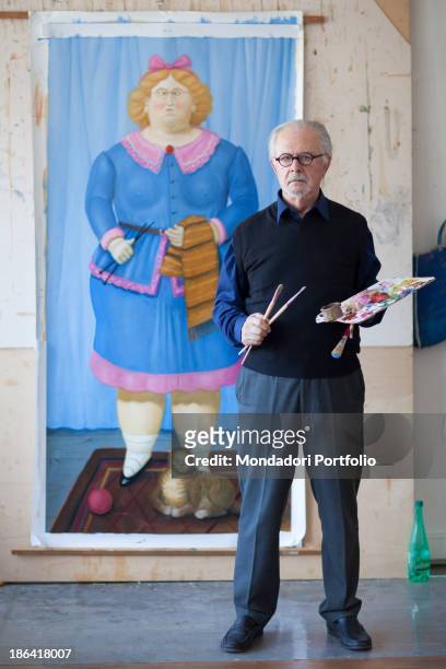 Colombian painter and sculptor Fernando Botero posing with paint brushes and palette in the hands in front of a painting depicting a female figure...