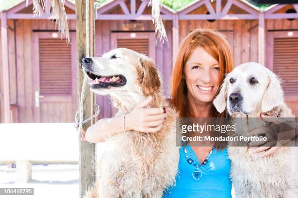 Italian politician and animalist Michela Vittoria Brambilla smiling between two Golden Retriever dogs in front of the bathing-huts at the lido Bau...