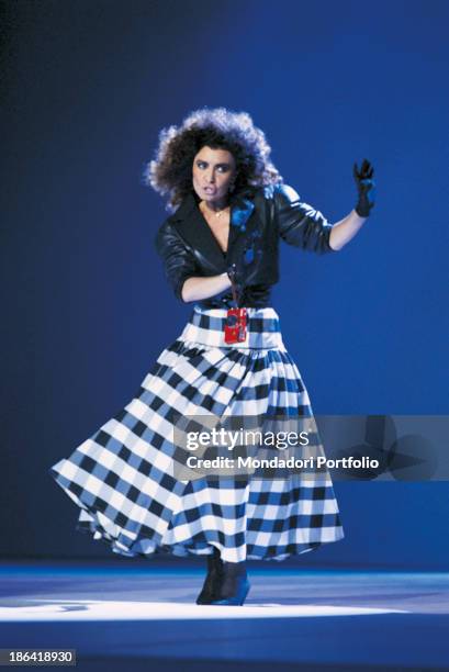 Italian singer Loredana Berté dancing wearing a long tartan skirt and a red camera at her wrist. 1986.