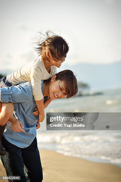 mother giving daughter a piggyback ride - toothy smile family outdoors stock pictures, royalty-free photos & images