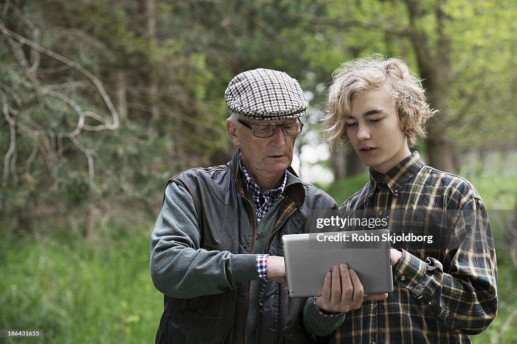 Elderly man and boy in forrest looking at tablet computer