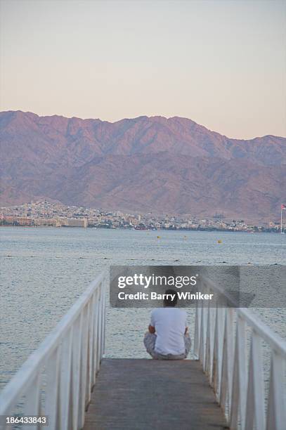 lone man sitting near water facing jordan - mer rouge photos et images de collection