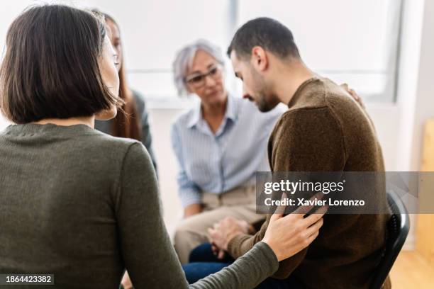 men and women with therapist sitting in a circle together during therapy group, supporting each other - substance abuse stock pictures, royalty-free photos & images
