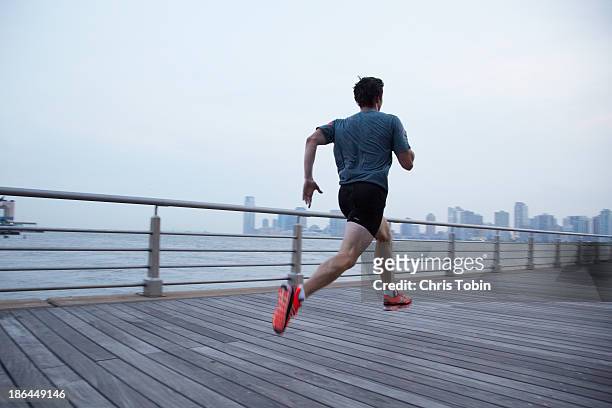 man running on pier in front of city skyline - man running city fotografías e imágenes de stock